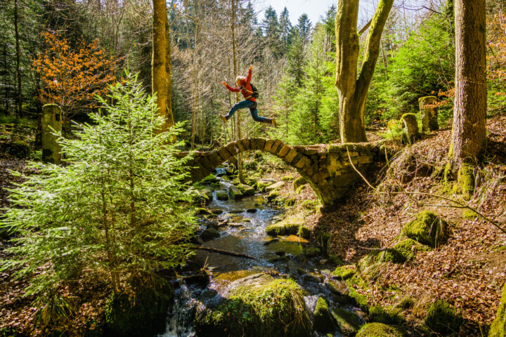 Mensch springt über kleine Brücke aus Stein mitten im Wald. Foto: ALEX KIJAK