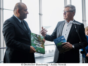 Bundestagsvizepräsident Omid Nouripour (l), Bündnis 90/Die Grünen, MdB, nimmt den Weihnachtsbaum des Naturparks Barnim entgegen. Hier während der Übergabe eines Buchgeschenks mit dem Landrat a. D. Friedel Heuwinkel (r), Präsident Verband Deutscher Naturparke e. V. © Deutscher Bundestag / Anika Nowak