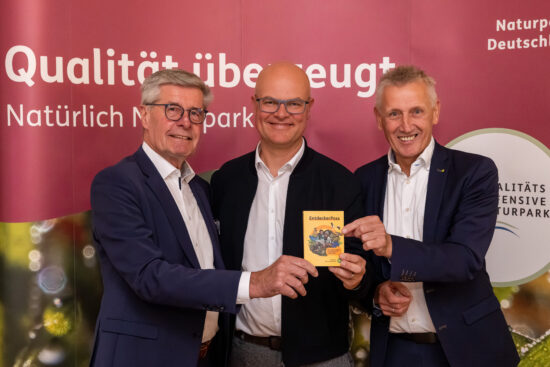 Umweltminister Tobias Goldschmidt (Mitte) bekam das bundesweit erste Exemplar des druckfrischen EntdeckerPasses im Naturpark Aukrug überreicht, in dem sich im handlichen Din A 5-Format alle Nationalen Naturlandschaften Deutschlands erstmals gemeinsam vorstellen. Überreicht wurde der EntdeckerPass von Friedel Heuwinkel, Präsident VDN e. V. (links), sowie von Peter Südbeck, Vorstandsvorsitzender von NNL e. V. © Jan Kulke