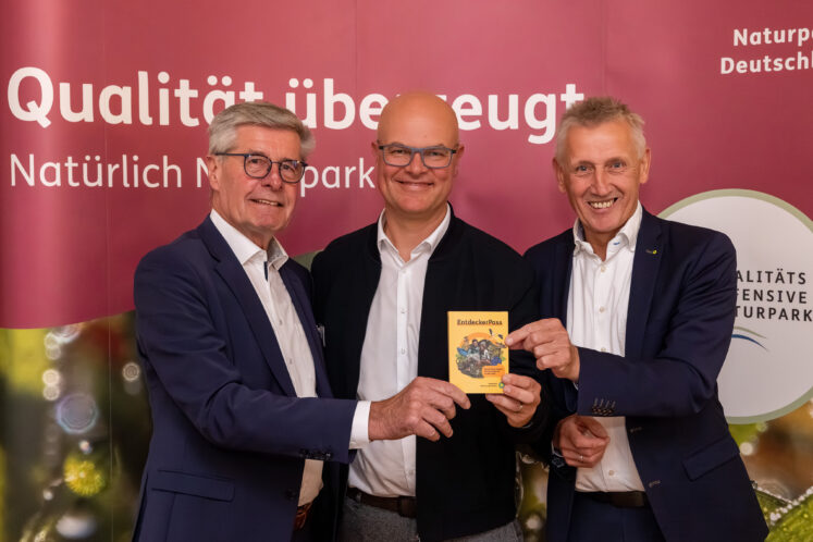 Umweltminister Tobias Goldschmidt (Mitte) bekam das bundesweit erste Exemplar des druckfrischen EntdeckerPasses im Naturpark Aukrug überreicht, in dem sich im handlichen Din A 5-Format alle Nationalen Naturlandschaften Deutschlands erstmals gemeinsam vorstellen. Überreicht wurde der EntdeckerPass von Friedel Heuwinkel, Präsident VDN e. V. (links), sowie von Peter Südbeck, Vorstandsvorsitzender von NNL e. V. © Jan Kulke